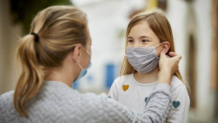 A mother wearing surgical mask helps daughter putting home made face mask during coronavirus pandemic.