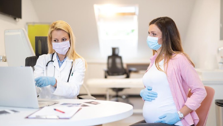 Young pregnant woman on a visit to doctor. Wearing protective masks and gloves during corona virus epidemic.