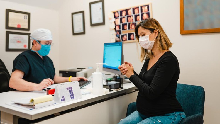 Young pregnant woman on a visit to doctor. Wearing protective masks and gloves during corona virus epidemic.