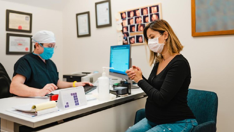 Hamil di tengah pandemi corona Young pregnant woman on a visit to doctor. Wearing protective masks and gloves during corona virus epidemic.