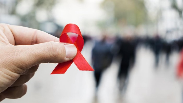 closeup of a red awareness ribbon for the fight against AIDS in the hand of a young caucasian man in a busy pedestrian street of a city