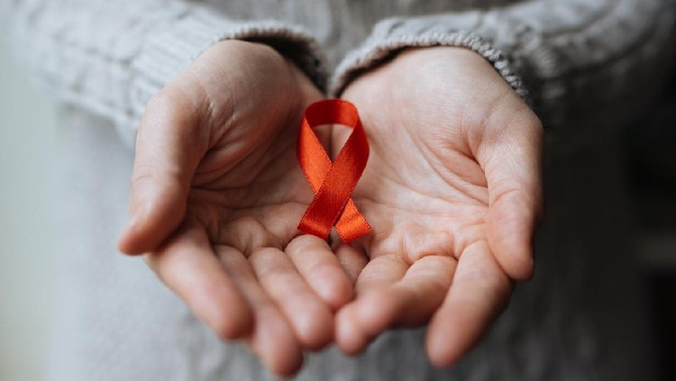 closeup of a red awareness ribbon for the fight against AIDS in the hand of a young caucasian man in a busy pedestrian street of a city