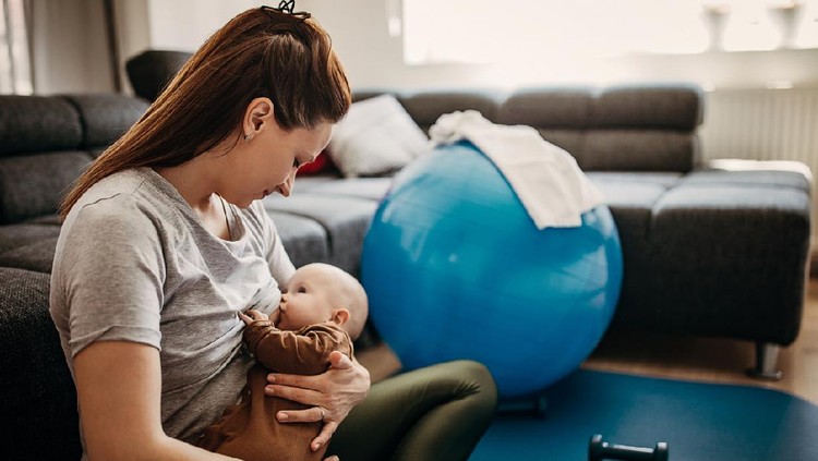 Two people, mother taking a break from exercising to breastfeed her baby son at home.