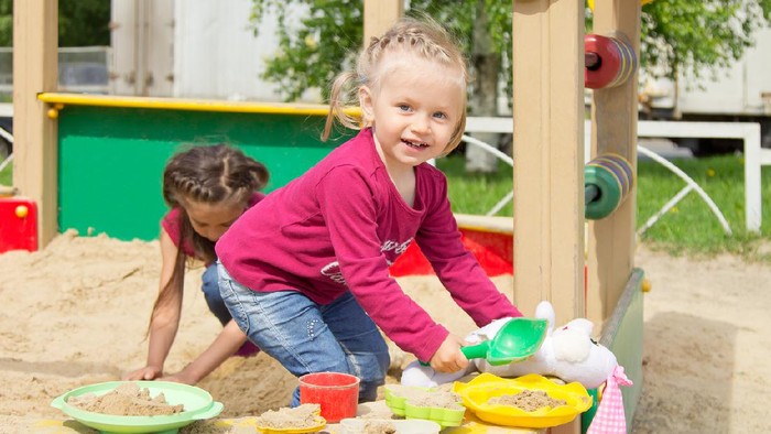 Adorable little girl playing in the sandbox on a playground