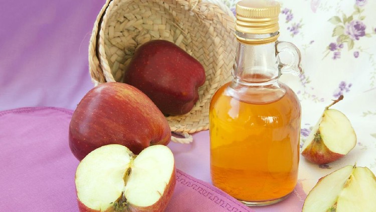 A glass bottle of red apple vinegar. Fresh red apples in the background.