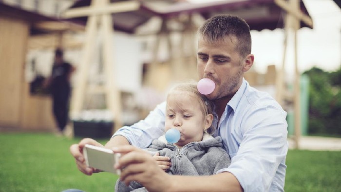 Father and his daughter are blowing bubble gum while they are taking selfles with a mobile phone. Candid shot.