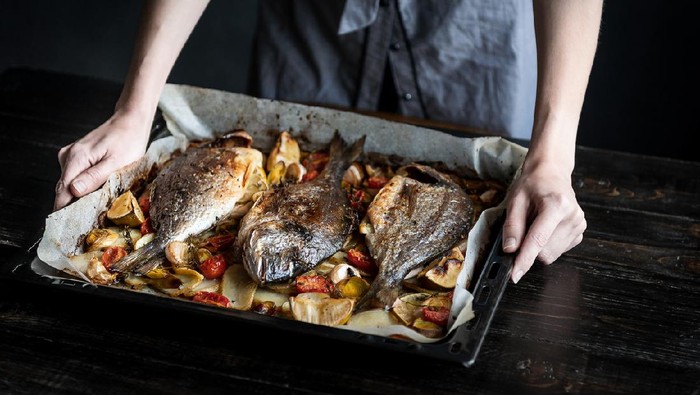 fish for dinner. in female hands baked fish on a baking sheet.