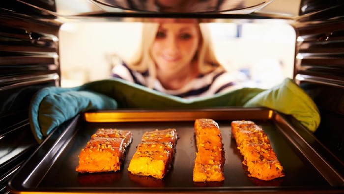 Woman Putting Salmon Fillets Into Oven To Cook.  Smiling