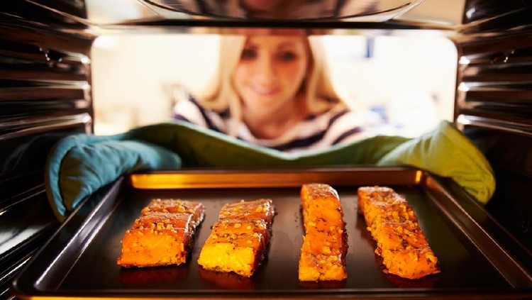 Woman Putting Salmon Fillets Into Oven To Cook.  Smiling
