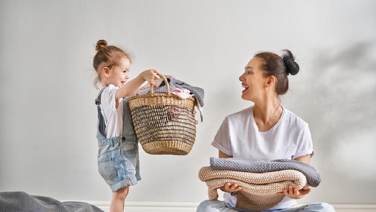 Beautiful young woman and child girl little helper are having fun and smiling while doing laundry at home.