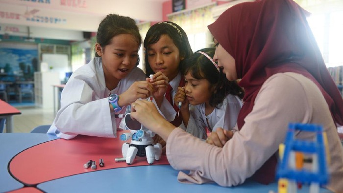 Asian elementary schoolgirls and female teacher building robot in science class