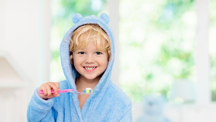 Child brushing teeth. Kids tooth brush and paste. Little baby boy in blue bath robe or towel brushing his teeth in white bathroom with window on sunny morning. Dental hygiene and heath for children.