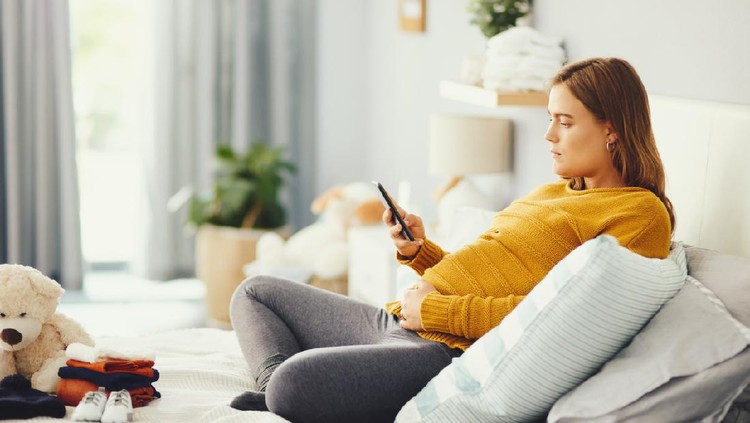 Shot of an attractive young pregnant woman using a cellphone while relaxing in her bedroom at home