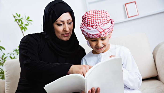Happy Arabic mother and son together sitting on the couch and reading a book.