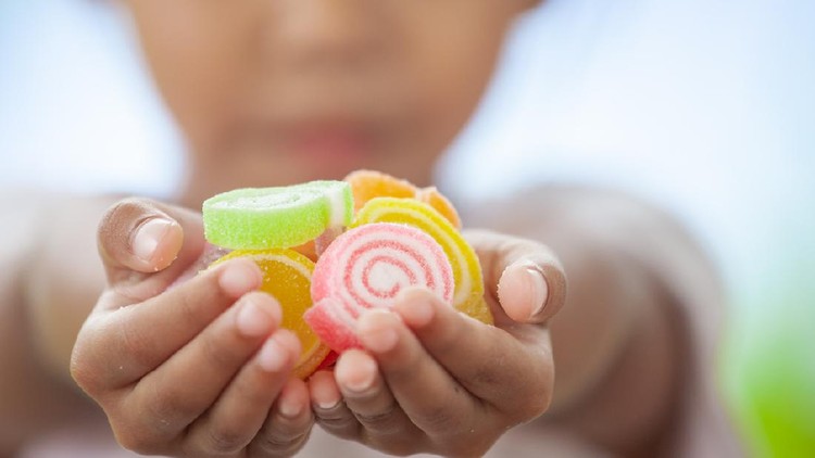 Cute asian child girl holding jelly candies in hand and sharing to other