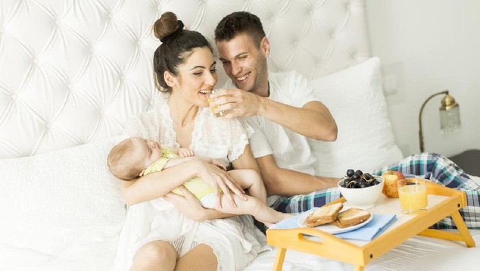 Young parents with baby girl having breakfast in bed