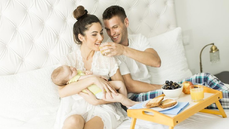 menyusui Young parents with baby girl having breakfast in bed
