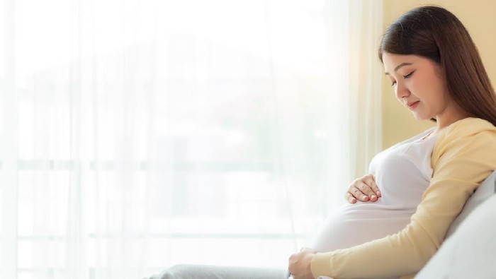 Happy pregnant mother touching and looking beautiful belly sitting on cozy bed at home. prenatal, pregnancy, motherhood, expect concept. Young pregnance girl care and love her baby. copy space