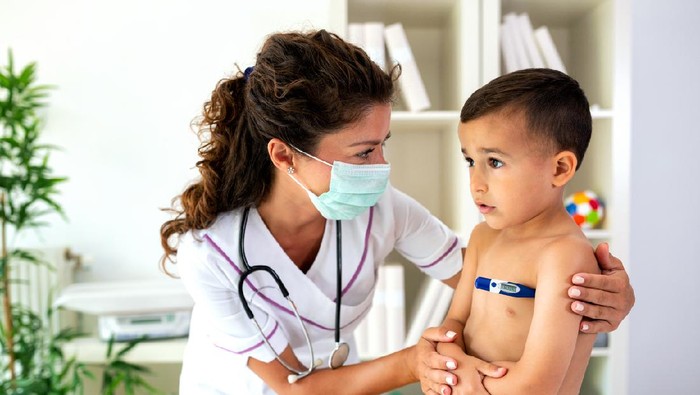 Doctor checking body temperature of young boy providing him with healthcare if needed