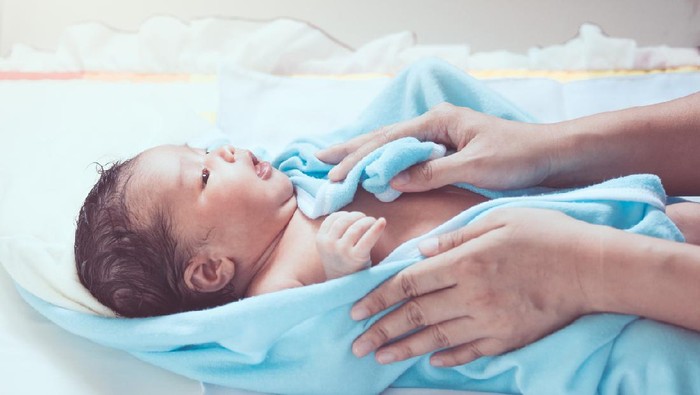 Cute newborn baby girl in towel after bath with mother hands rub her body dry with tenderness