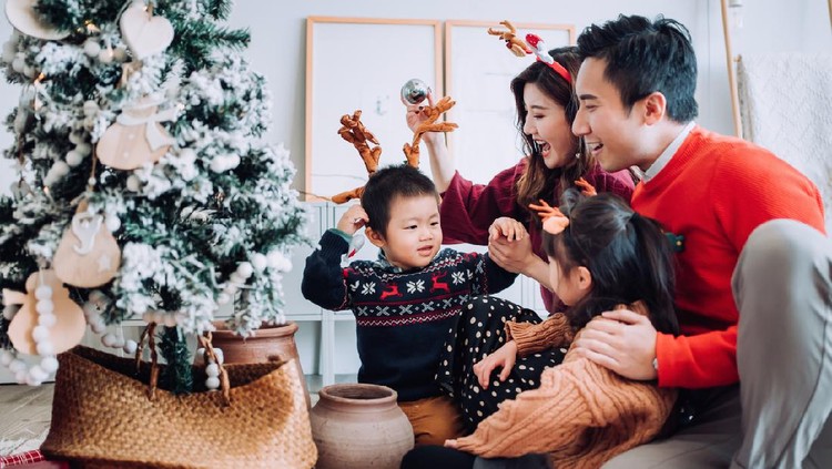 Christmas lifestyle theme. Happy Asian family decorating Christmas tree together in the living room at home. They are putting on various baubles and ornaments and enjoying their holiday