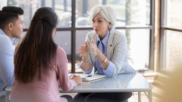 Serious Caucasian senior female counselor gestures while giving important advice to a young married couple.