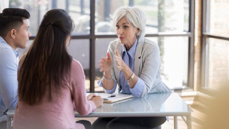 Serious Caucasian senior female counselor gestures while giving important advice to a young married couple.