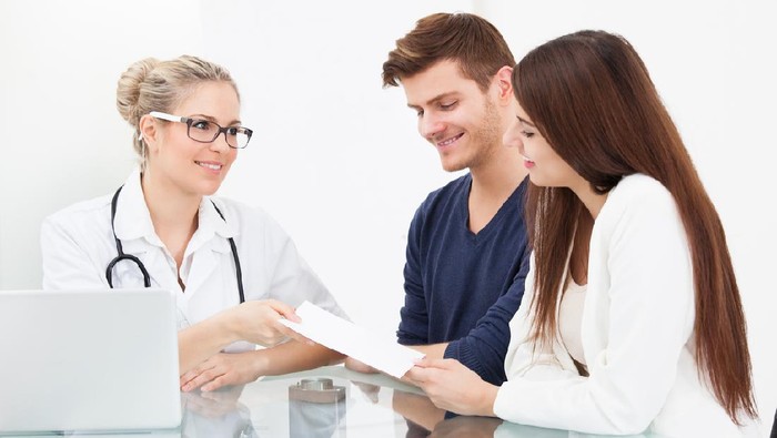 Female doctor giving prescription paper to couple at desk in clinic