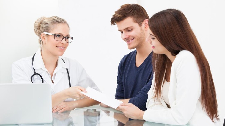 Female doctor giving prescription paper to couple at desk in clinic