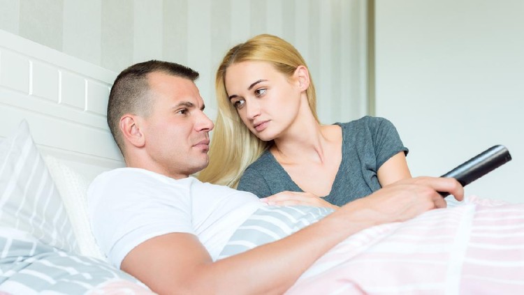Young attractive caucasian couple in bed. Man watching tv, woman lovingly looking at him, hoping to catch his attention.