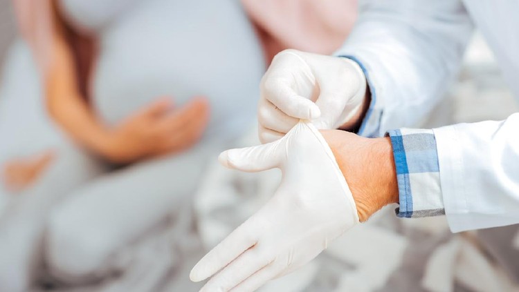 Do not worry. Male physician examining pulse of an expectant mother during an appointment at clinic.