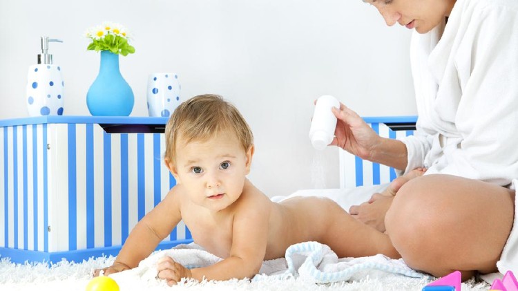 Mother pampering her baby girl daughter at home, applying baby powder to her body. Real people, mother 30-35, baby girl 10 months.