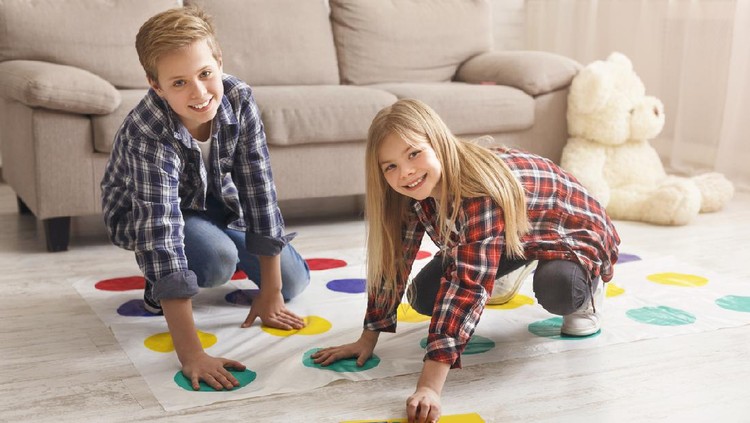 Cheerful siblings playing twister game on floor having fun at home on weekend. Kids friendship and leisure activities.