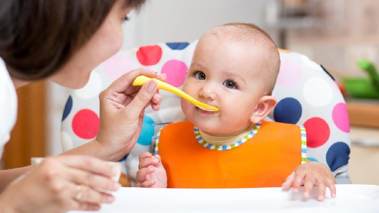 Anak makan smiling baby girl eating food with mom on kitchen