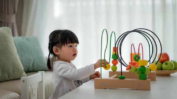 Adorable Asian Toddler baby girl sitting on chair and playing with color developmental toys at home.
