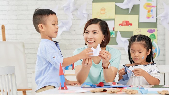 Young Asian woman teaching children how to make paper ships at art craft