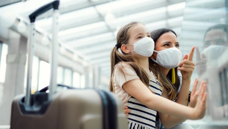 Young mother with daughter going on holiday, wearing face masks at the airport.