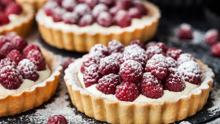 Delicious raspberry mini tarts (tartlets) with whipped cream on dark background