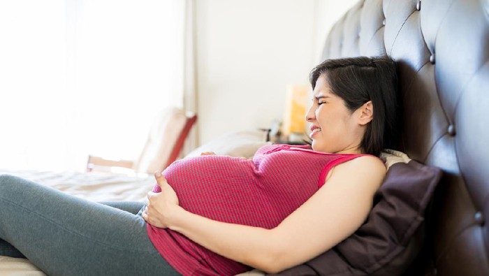Side view of stressed woman getting regular contractions on bed