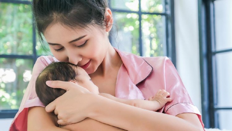 Asian mother holding a 1.5-month-old child, leaning over her shoulder