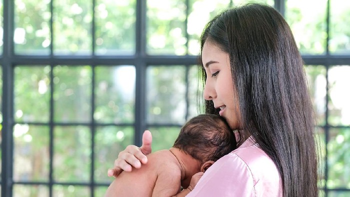 Asian mother holding a 1.5-month-old child, leaning over her shoulder