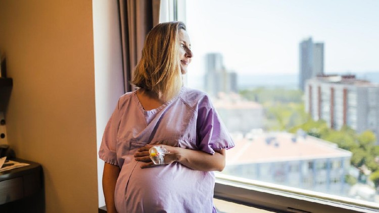 hamil Young Pregnant woman touching stomach while waiting Travail towards window at hospital ward