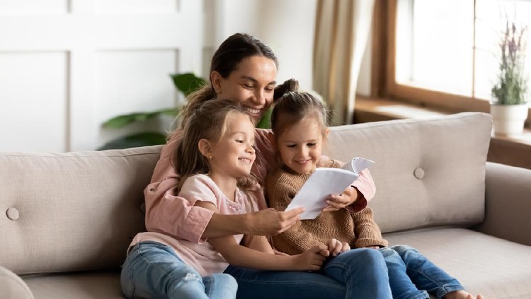 mendongeng Happy family young mother babysitter hold read book relax embrace cute little children daughters, smiling parent mum tell small kids funny fairy tale story sit on sofa having fun together at home