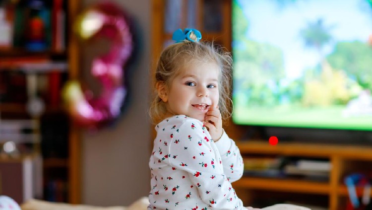 Cute little toddler girl in nightwear pajamas watching cartoons or movie on tv. Happy healthy baby child at home