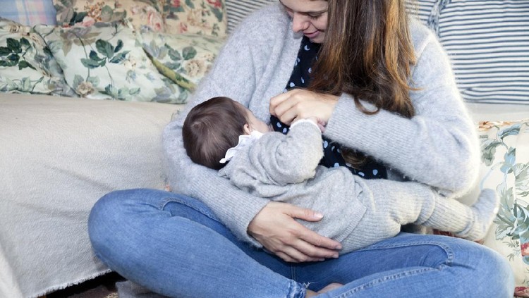 1205260201 Mother breastfeeding her baby boy in arms, sitting on bed.