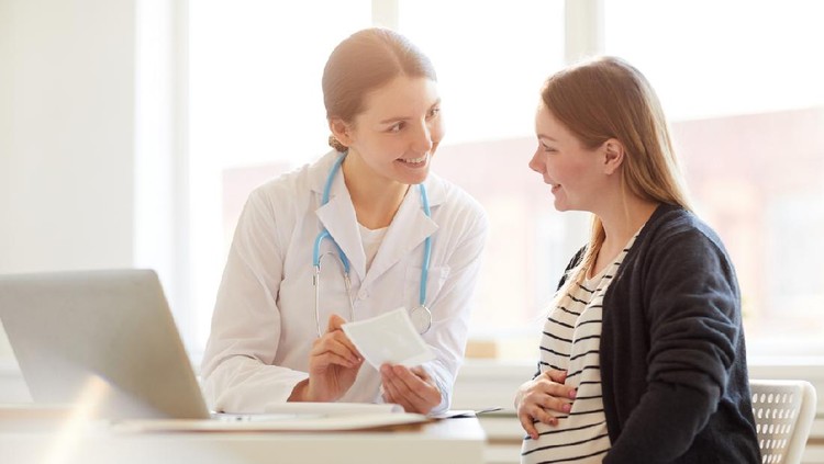 Portrait of female obstetrician smiling at pregnant woman in doctors office, copy space