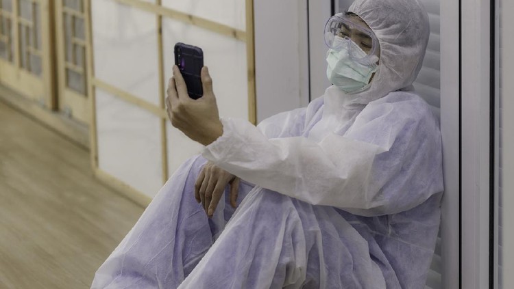 1282442532 young Asian doctor, dressed in anti-virus clothing, sits on the floor tired and uses a smartphone to make a video call to his family. corona virus concept.
