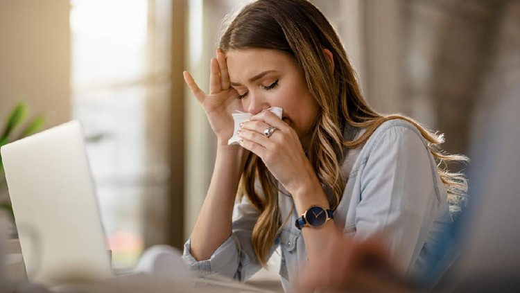 Young businesswoman with clpd and flu virus blowing nose while working in the office.