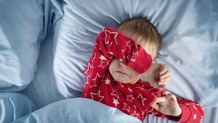 Sleepy boy lying in bed with blue beddings. Tired child in bedroom. Little kid lying awake in red pajamas with toothacheSleepy boy lying in bed with blue beddings. Tired child in bedroom sleeping. Little kid lying asleep in red pajamas with alarm clock