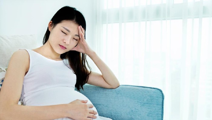 Pregnant woman sitting on sofa and having headache